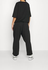 Schwarzes, übergroßes T-Shirt und dazu passende, lockere Hose aus weichem Stoff, mit gerippten Bündchen und Sneakers mit grauen Akzenten.