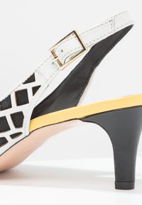 Černobílé slingback podpatky s výřezovými geometrickými vzory, žlutou stélkou a třicetimilimetrovým černým podpatkem s texturovaným povrchem.