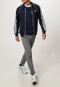 Námornícky zipový sportovní bunda s bílými pruhy, kombinovaná s navy tričkem a šedými kalhotami. Doplňena o bílé tenisky s zelenými akcenty.