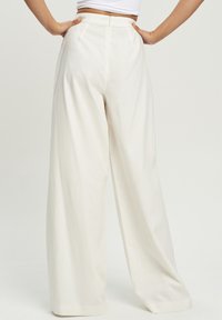 Szerokie spodnie w kremowym kolorze, z wysokim stanem, bocznymi plisami i ukrytym zamkiem błyskawicznym z tyłu dla czystego wykończenia.