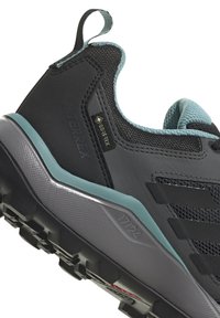 Czarne buty turystyczne z teksturowaną cholewką, akcentami w kolorze teal, brandingiem Gore-Tex oraz szarym spodem z wyraźnym bieżnikiem i wzorami.
