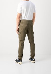 Spodnie cargo w oliwkowym kolorze z elastycznym paskiem w talii, zwężanymi nogawkami, kieszeniami bocznymi i tylnymi, w połączeniu z gładką białą koszulką i trampkami.