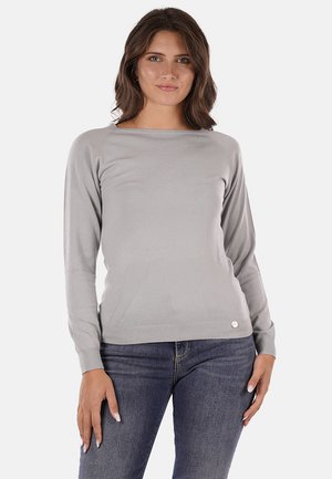 Maglione grigio a maniche lunghe con scollo a barca, di tessuto a costine, e un piccolo logo in basso. Indossato con jeans blu.