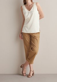 Top senza maniche beige chiaro con scollatura a V, abbinato a pantaloni cropped color cammello e sandali con tacco a motivo. Texture semplice e liscia.