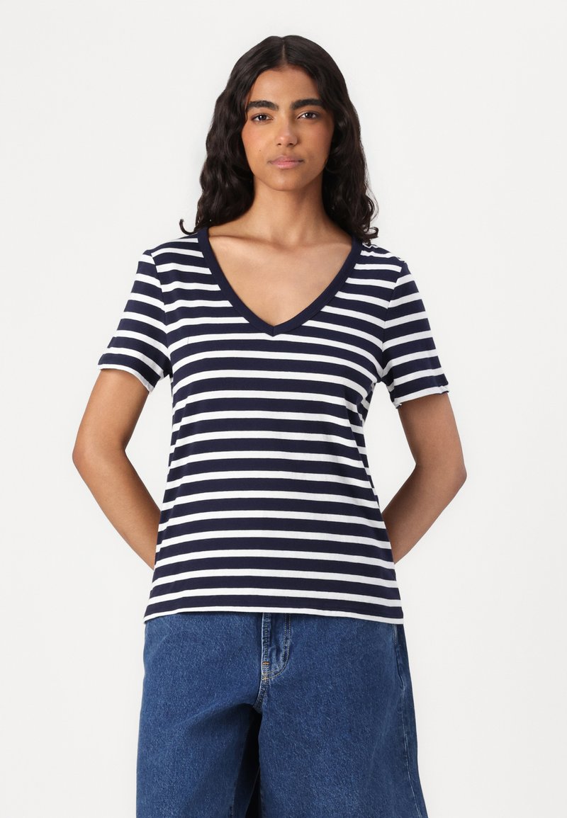 Niebiesko-białe paski na koszulce z dekoltem w serek, krótkim rękawkiem i miękkiego materiału. Zestawiona z jasnoniebieskimi, luźnymi szortami dżinsowymi.