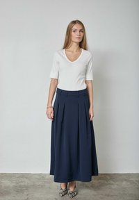 Top blanco de manga corta con textura acanalada y escote en V combinado con una falda larga plisada en azul marino, acompañado de zapatos de tacón alto con estampado.