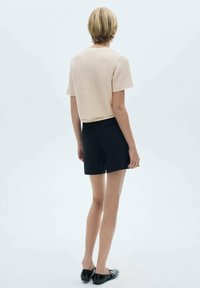 Jasnoróżowa, teksturowana bluzka dzianinowa z krótkimi rękawami, zestawiona z czarnymi szortami. Plecy modelki są widoczne, ukazując prosty krój i prosty dół.