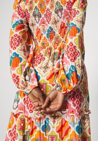 Farverig bomulds kjole med livlige geometriske mønstre i pink, orange og blå, med smocket forparti og flæser i kanten.