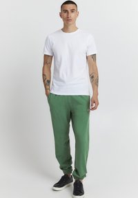 Grønne joggebukser med elastiske mansjetter, med en logoaccent. Kombinert med en enkel hvit t-skjorte med rund hals og svarte joggesko.