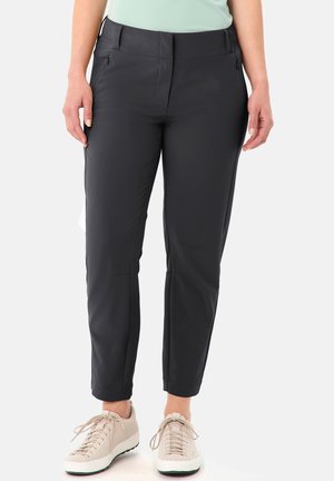 Pantalon noir coupe slim avec poches latérales zippées porté par une personne en baskets beiges et haut vert clair, debout sur fond blanc.