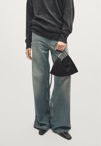 Wide-legged light blue jeans made of denim, paired with a black ribbed sweater and a textured black suede bag, featuring a curved shape.