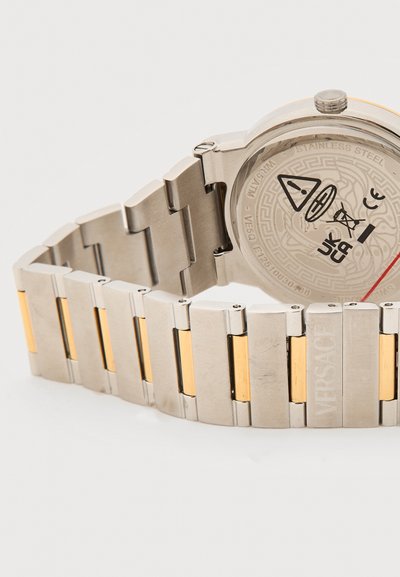 Λουρί ρολογιού δίχρωμο από ανοξείδωτο ατσάλι και χρυσό με εγχάραγμα του λογότυπου Versace, που δείχνει την πίσω πλευρά με σύμβολα ασφαλείας και πιστοποίησης.