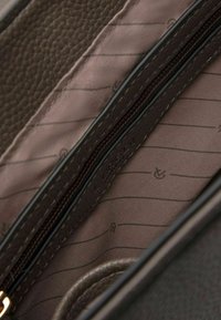 Interieur van een bruine leren handtas met een textuurafwerking, met een ritszak en een gladde, gestreepte stofvoering.