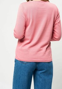 Maglione rosa con una texture morbida e maniche lunghe, abbinato a jeans blu. Il design presenta un collo rotondo e una vita aderente.