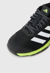 Black athletic shoe with mesh upper, three white stripes, gray laces, and a green accent on the sole. Features a dual density design.