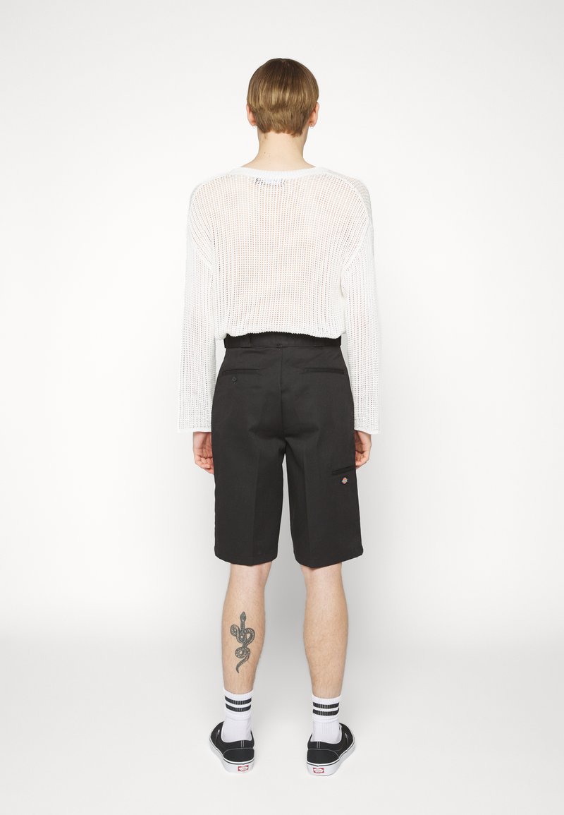 Black shorts with a relaxed fit and back pockets. Paired with a white, open-knit sweater. Footwear: black slip-ons with white accents.