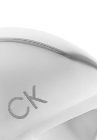 Silbernes Metallaccessoire mit einem glatten, abgerundeten Design. Verfügt über das eingeätzte "CK"-Logo und eine subtile Kurve, die das elegante Finish hervorhebt.