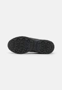 Gumová podrážka černé boty Asics s hlubokými vzory pro trakci, zobrazená na bílém pozadí.