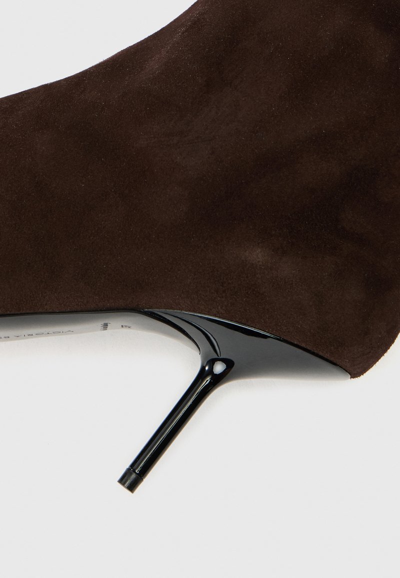 Brune ruskinds højhælet sko med en blank sort stiletto hæl. Designet har en glat tekstur og en spids tå.