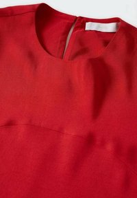 Robe en tissu rouge avec encolure ronde, fente au dos et étiquette blanche visible à l'intérieur du col sur fond blanc uni.