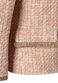Veste en tissu texturé avec des accents orange et vert, ornée d'un ourlet à franges et de détails en fil complexes.