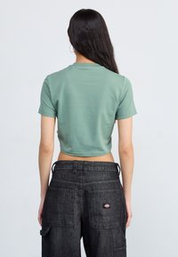 Cropped green T-shirt with short sleeves; paired with high-waisted dark gray cargo pants featuring large rear pockets and a logo patch.