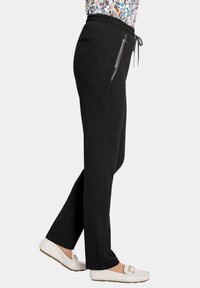 Zwarte joggingsbroek met een taps toelopend ontwerp, elastische tailleband, trekkoord en zijzakken met rits. Gladde stof met een lichte glans.