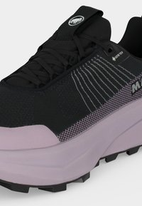 Μαύρο και γκρι παπούτσι Gore-Tex με παχιά ανοιχτό μωβ σόλα, σχεδιασμένο επάνω μέρος από δίχτυ και λογότυπο στη γλώσσα και στο πλαϊνό πάνελ.