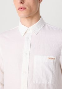 Camicia bianca con bottoni, realizzata in tessuto leggero, con taschino sul lato sinistro del petto con il logo arancione "Calvin Klein" e colletto classico.