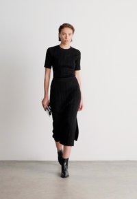 Rochie tricotată neagră, cu mânici scurte, silueta ajustată și lungime midi. Prezintă o fanta laterală și este asortată cu bocanci negri până la glezne.