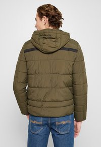 Olijfgroene pufferjas met een capuchon, met een horizontale gestikte textuur en een zwarte accentstreep over de bovenrug.