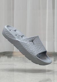 Sivi papučasti sandala izrađeni od teksturiranog materijala, s širokim otvorom i rupama za ventilaciju, s malim logotipom sa strane.