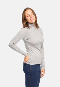 Maglione grigio a maniche lunghe con collo alto e vestibilità slim, realizzato in tessuto morbido. Indossato con jeans blu scuro con una striscia laterale luccicante.