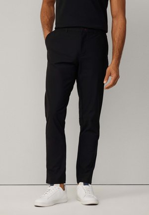 Black, slim-fit trousers made of smooth fabric, featuring side pockets and belt loops. Paired with white sneakers.