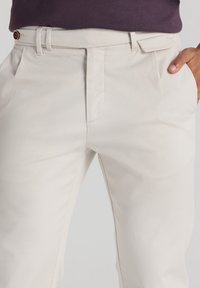 Pantalones de algodón beige con frente plano, pasadores para cinturón y bolsillos laterales. La tela tiene una textura suave, un corte entallado y un diseño minimalista.