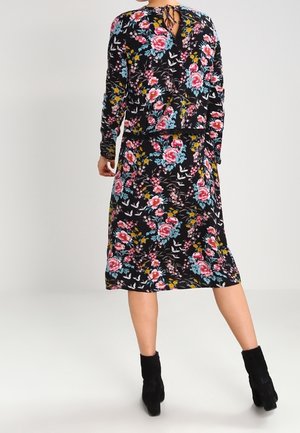 Vestido floral con manga larga, fondo negro, flores coloridas en rosa, azul y amarillo. Presenta un detalle en la parte posterior con lazo y un diseño hasta la rodilla.