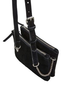 Sac bandoulière en suede noir avec deux compartiments zippés, une sangle ajustable et un accent en chaîne argentée. Présente des lignes épurées et un minimum de matériel.