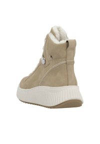 Beige suède enkellaars met een pluizige voering, witte gestructureerde zool en zilveren hardware accenten. Ronde neus en gepolsterde kraag voor comfort.