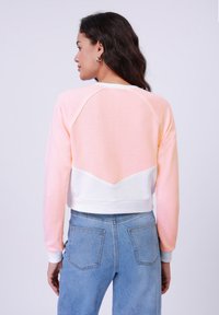 Krátký rukáv mikina v růžové a bílé barvě. Disponuje raglánovým designem s texturovaným povrchem a bílým v-švem na zadní straně.