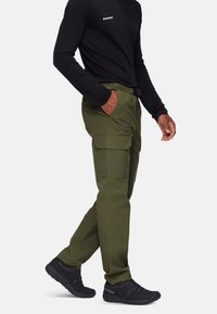 Olijfgroene cargobroek met meerdere zijzakken, elastische tailleband en slim fit, gecombineerd met zwarte sportschoenen en een zwarte longsleeve.