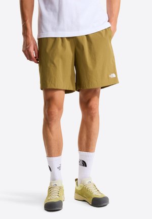 Olive green shorts with a lightweight, textured fabric. Features a small white logo on the left leg. Paired with white socks and light shoes.