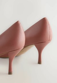 Scarpe con tacchi alti in pelle rosa, con punta affusolata e tacco affusolato. Texture liscia, parte posteriore angolata e nessun abbellimento visibile.