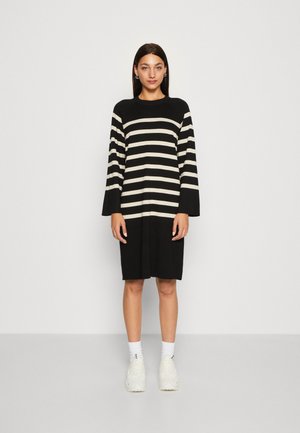Schwarz-weiß gestreiftes Kleid mit Rundhalsausschnitt und Glockenärmeln, aus gestricktem Stoff, knielang, getragen mit weißen Sneakern und Socken.