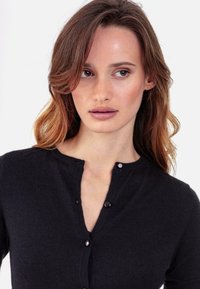 Schwarzer Strickcardigan mit rundem Halsausschnitt, ausgestattet mit kleinen runden Knöpfen und einer weichen Textur. Nahaufnahme des Oberbekleidungsteils.