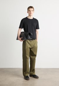 Svart t-skjorte med kort erm og lomme; olivengrønne løstsittende bukser; svart skinnveske; mørke sko; minimalisk design.
