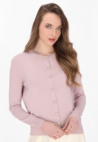 Cardigan roz deschis, realizat dintr-un material moale, cu o guler rotund și șapte butoane asemănătoare perlelor pe partea din față. Mâneci lungi și formă ajustată.