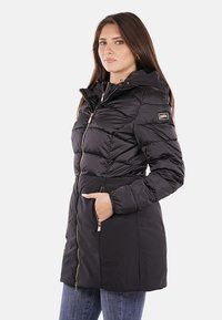 Giacca a vento nera con cappuccio, chiusura con zip e tasche. Presenta una texture trapuntata e una patch con logo sulla manica sinistra.