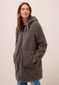Manteau en polaire gris avec une capuche, fermeture éclair frontale, deux grandes poches et cordons de serrage. Tissu doux et texturé, design mi-long.