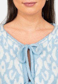 Cardigan a maglia di colore azzurro chiaro con stampa animale bianca, dotato di scollatura a v e chiusura annodata sul davanti. Texture morbida.