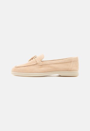 Beige suede loafer with low rubber sole, moccasin stitching, and decorative gold-tone buckle on top, shown in side profile.